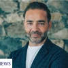 Yiannis Misirlis, Chairman at Imperio Group and LBDA, dressed in a dark blue jacket, standing in front of a stone wall