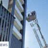 Firefighters conduct a high-rise rescue drill using an aerial platform outside a modern residential building.